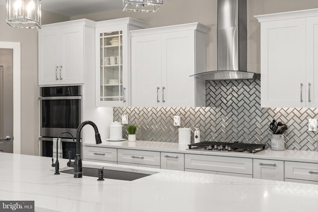 kitchen with sink, wall chimney exhaust hood, stainless steel appliances, tasteful backsplash, and white cabinets