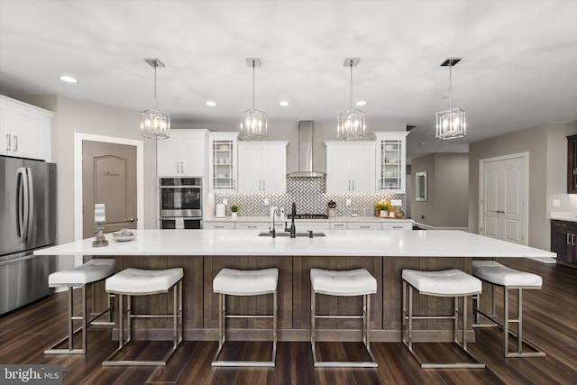 kitchen featuring a large island, wall chimney exhaust hood, stainless steel appliances, and decorative light fixtures