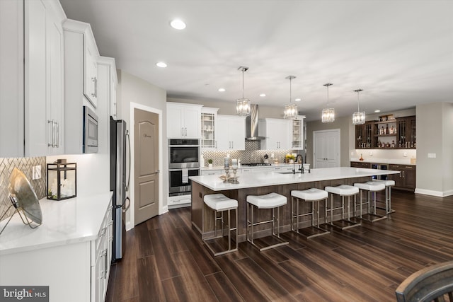 kitchen featuring wall chimney exhaust hood, dark hardwood / wood-style flooring, a kitchen island with sink, white cabinets, and appliances with stainless steel finishes