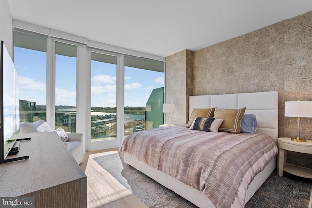 bedroom with hardwood / wood-style floors, access to outside, and a water view