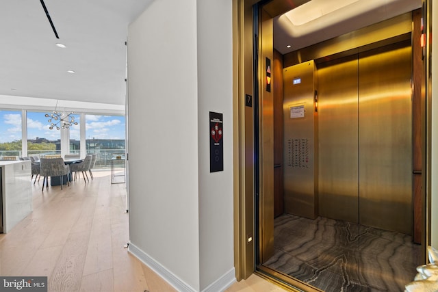 corridor with elevator, a chandelier, and light wood-type flooring