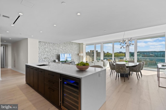 kitchen with light hardwood / wood-style floors, a kitchen island with sink, sink, and wine cooler