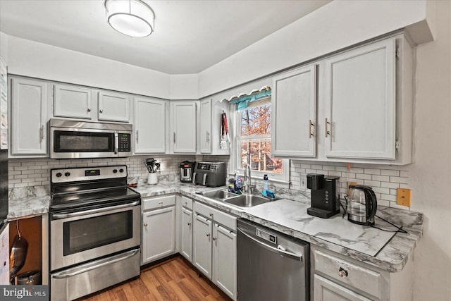 kitchen with sink, light stone counters, backsplash, light hardwood / wood-style floors, and appliances with stainless steel finishes