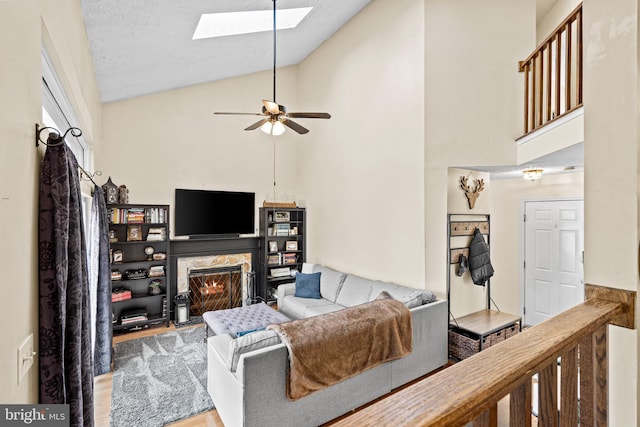 living room featuring a high end fireplace, a skylight, ceiling fan, light hardwood / wood-style flooring, and high vaulted ceiling