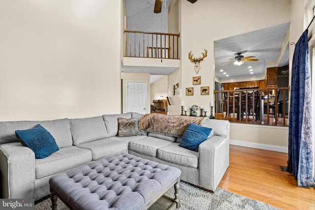 living room with ceiling fan, light wood-type flooring, and a towering ceiling