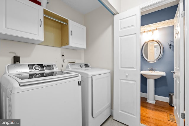 laundry area with cabinets, light hardwood / wood-style floors, washer and clothes dryer, and sink