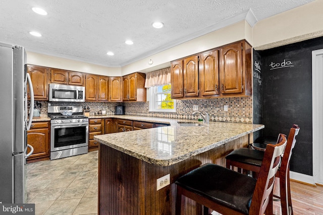 kitchen featuring sink, stainless steel appliances, kitchen peninsula, decorative backsplash, and a breakfast bar