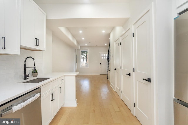 kitchen featuring appliances with stainless steel finishes, light wood-type flooring, backsplash, sink, and white cabinetry