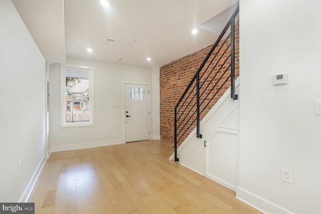 foyer with light hardwood / wood-style floors and brick wall