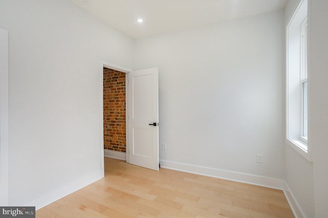 empty room with light hardwood / wood-style flooring and brick wall