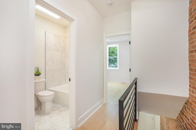 bathroom featuring bathtub / shower combination, hardwood / wood-style flooring, toilet, and brick wall