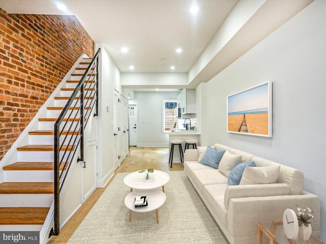 living room with sink, brick wall, and light wood-type flooring