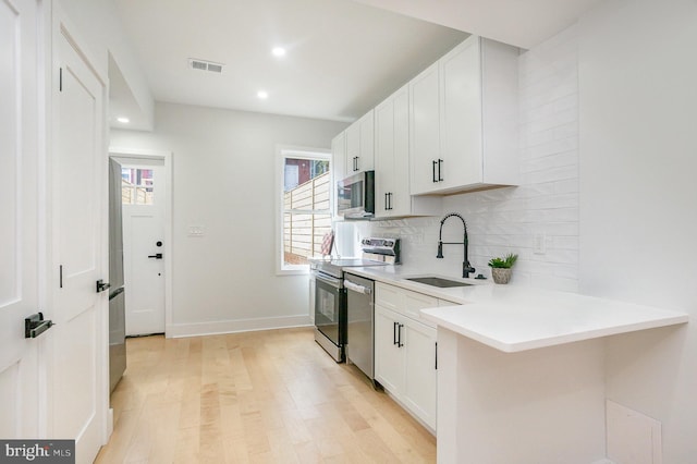 kitchen featuring kitchen peninsula, appliances with stainless steel finishes, light wood-type flooring, sink, and white cabinetry