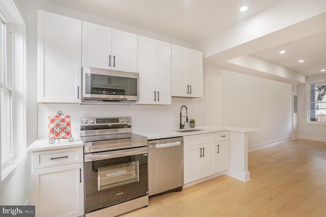 kitchen featuring white cabinetry, sink, backsplash, appliances with stainless steel finishes, and light wood-type flooring