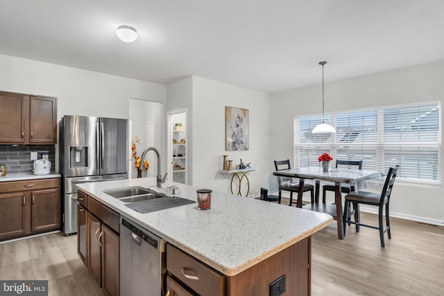 kitchen with sink, an island with sink, stainless steel appliances, and light wood-type flooring