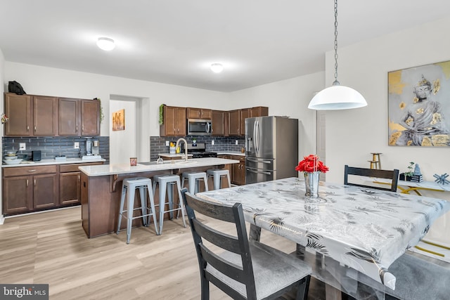 kitchen featuring pendant lighting, backsplash, stainless steel appliances, and light hardwood / wood-style flooring