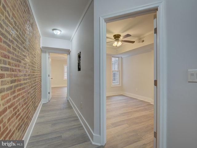 corridor with light hardwood / wood-style flooring, brick wall, and ornamental molding