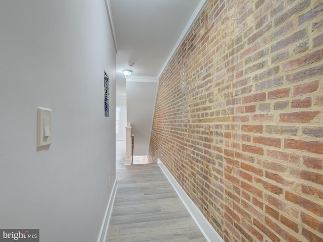 corridor with light hardwood / wood-style floors, ornamental molding, and brick wall