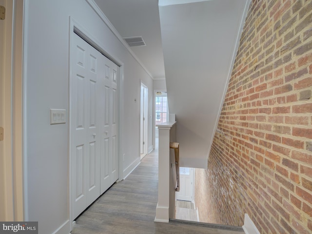 corridor featuring light hardwood / wood-style flooring, ornamental molding, and brick wall