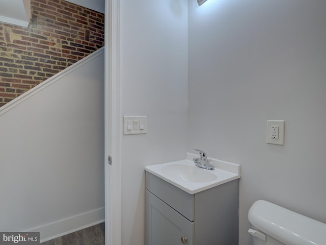 bathroom with hardwood / wood-style floors, vanity, toilet, and brick wall