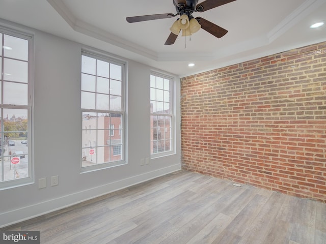 empty room featuring ceiling fan, a tray ceiling, brick wall, and light hardwood / wood-style flooring