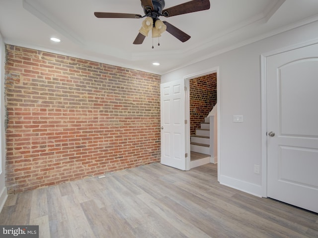 empty room with ceiling fan, ornamental molding, brick wall, and light hardwood / wood-style floors