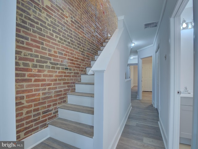 stairway featuring wood-type flooring and brick wall