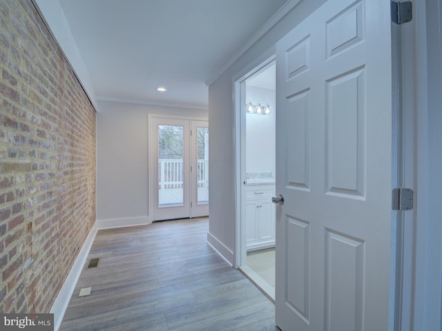 hallway featuring light hardwood / wood-style floors, ornamental molding, and brick wall