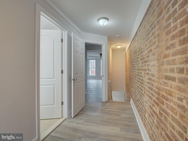 hallway with light hardwood / wood-style floors, crown molding, and brick wall