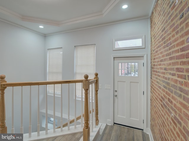 foyer featuring hardwood / wood-style flooring, ornamental molding, and brick wall