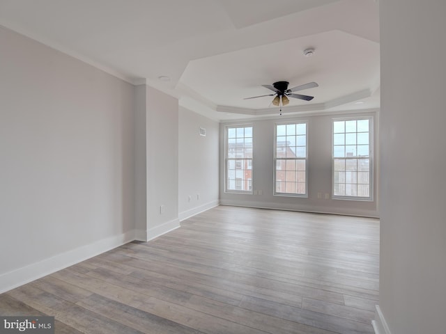 empty room with ceiling fan, light hardwood / wood-style floors, and a raised ceiling