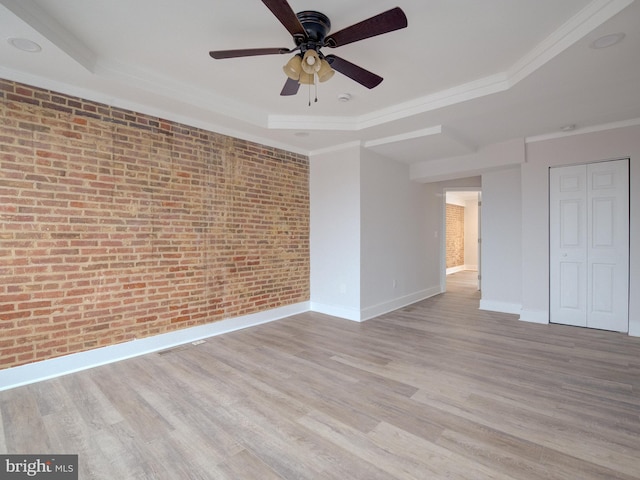 spare room featuring a tray ceiling, brick wall, and light hardwood / wood-style floors