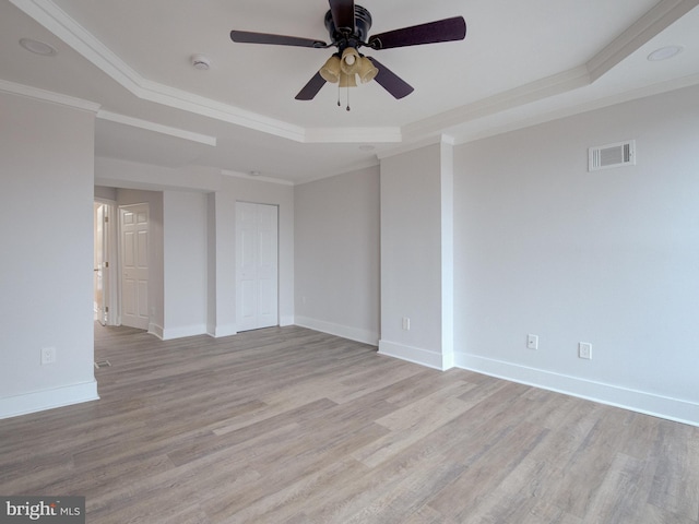 unfurnished room with ceiling fan, a raised ceiling, light wood-type flooring, and crown molding