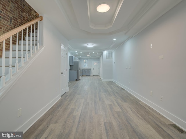 hall featuring hardwood / wood-style flooring, a raised ceiling, crown molding, and brick wall