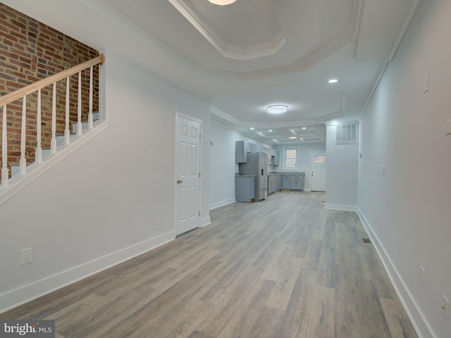 unfurnished living room featuring crown molding, a tray ceiling, and light hardwood / wood-style flooring