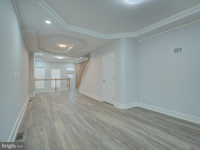 empty room featuring a tray ceiling, ornamental molding, and light wood-type flooring