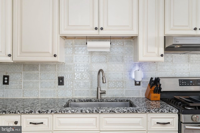 kitchen with decorative backsplash, dark stone counters, sink, exhaust hood, and stainless steel stove