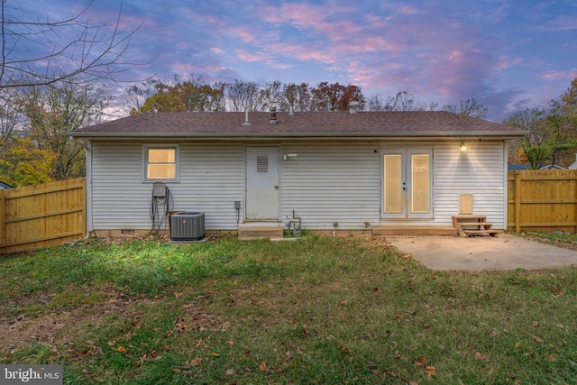 back house at dusk featuring a lawn, a patio, and central AC