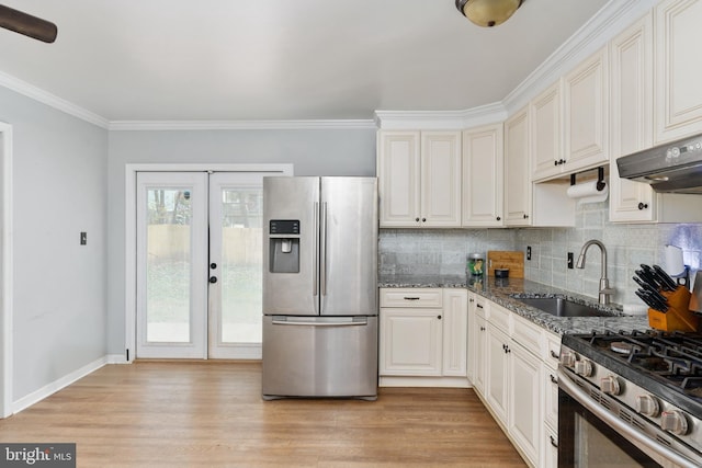 kitchen featuring ornamental molding, dark stone counters, stainless steel appliances, sink, and light hardwood / wood-style flooring