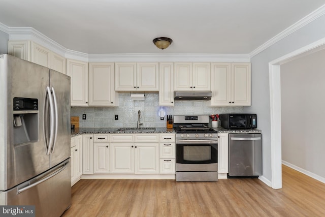 kitchen with sink, stainless steel appliances, tasteful backsplash, dark stone countertops, and light wood-type flooring