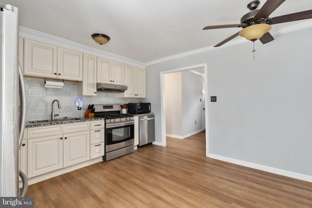 kitchen with appliances with stainless steel finishes, ceiling fan, sink, light hardwood / wood-style flooring, and dark stone countertops