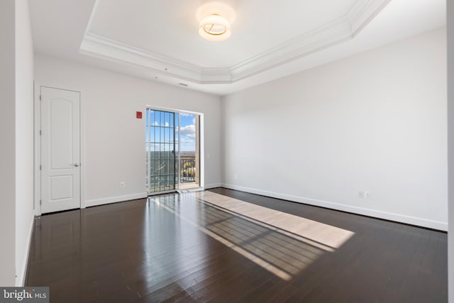 empty room featuring ornamental molding, a tray ceiling, and dark wood-type flooring