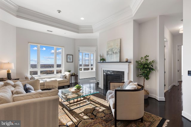 living room featuring a tray ceiling, a premium fireplace, crown molding, and dark wood-type flooring