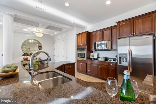 kitchen featuring beam ceiling, sink, decorative columns, dark stone countertops, and appliances with stainless steel finishes