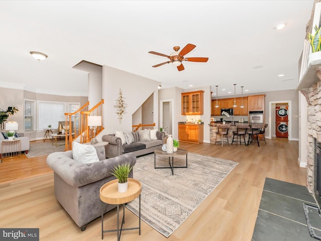 living room featuring light wood-type flooring, a stone fireplace, and ceiling fan