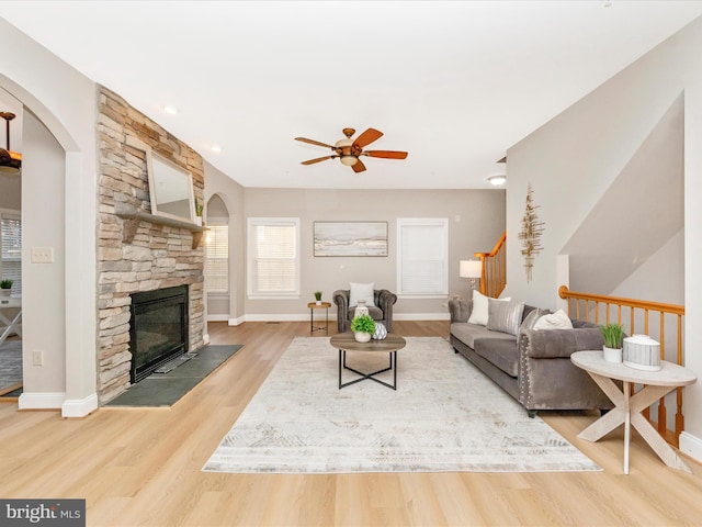 living room with a stone fireplace, ceiling fan, and hardwood / wood-style floors