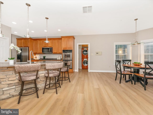 kitchen featuring a kitchen bar, appliances with stainless steel finishes, light wood-type flooring, decorative light fixtures, and stacked washer / dryer