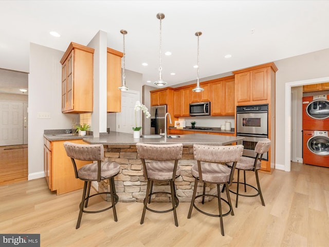 kitchen featuring stainless steel appliances, sink, light hardwood / wood-style flooring, stacked washer and clothes dryer, and hanging light fixtures