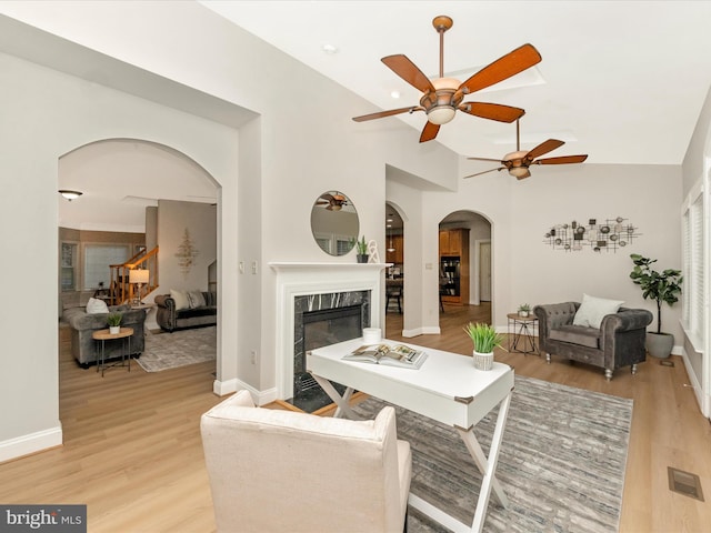 living room featuring a premium fireplace, ceiling fan, light hardwood / wood-style floors, and vaulted ceiling