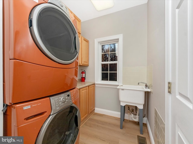 laundry room featuring stacked washer / drying machine, cabinets, and light hardwood / wood-style flooring